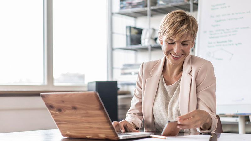 woman sat at desk working on laptop and mobile phone